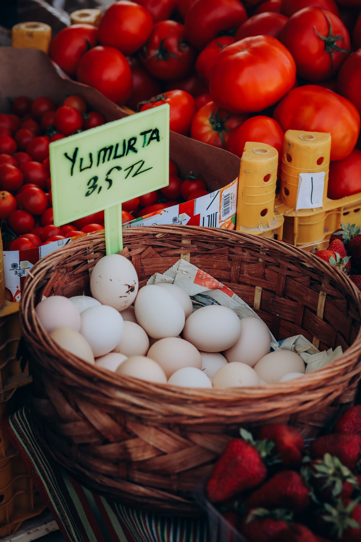 Wicker basket of eggs amid fresh tomatoes and strawberries at Balıkesir market.